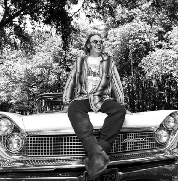 Neil Young on the hood of a big ol' tank of a car
